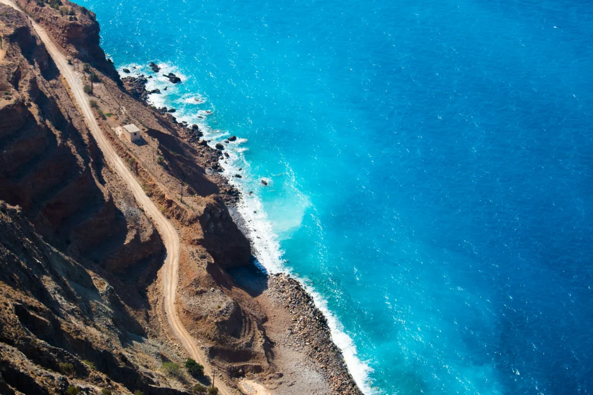 Cretan cliffs meeting a turquoise sea, a dirt road winding down.