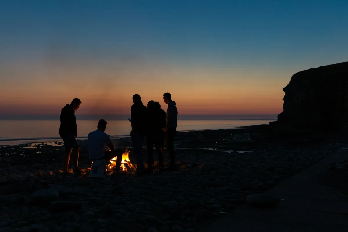 People gathered around a small fire on a beach at dusk.